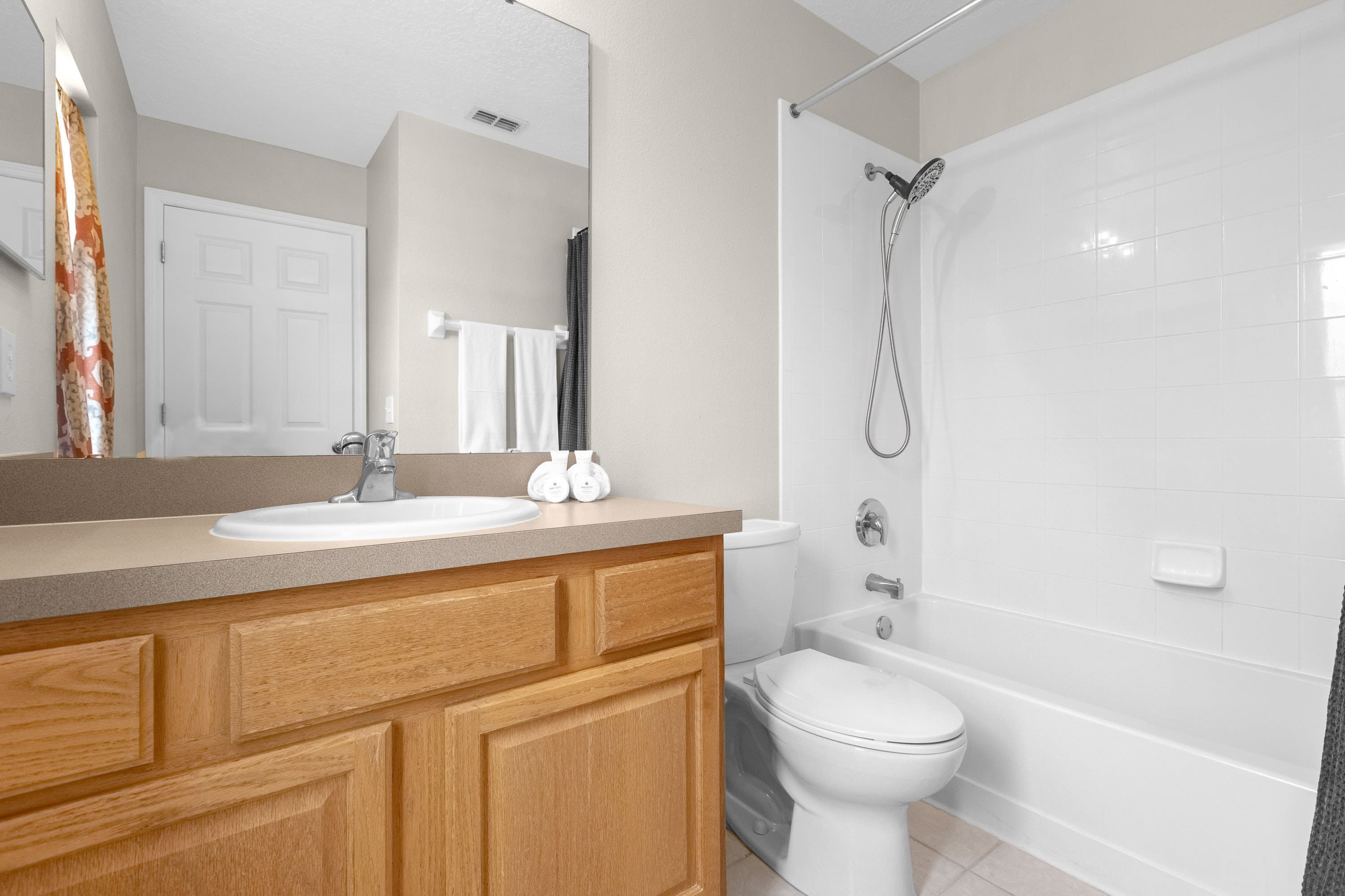 A modern bathroom with a wooden vanity, white sink, and a shower area.