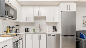 A modern kitchen with white cabinets, a stainless steel refrigerator, a dishwasher, and a microwave. - Stylish 1BR Condo w Balcony Skyline Views (Kitchener)