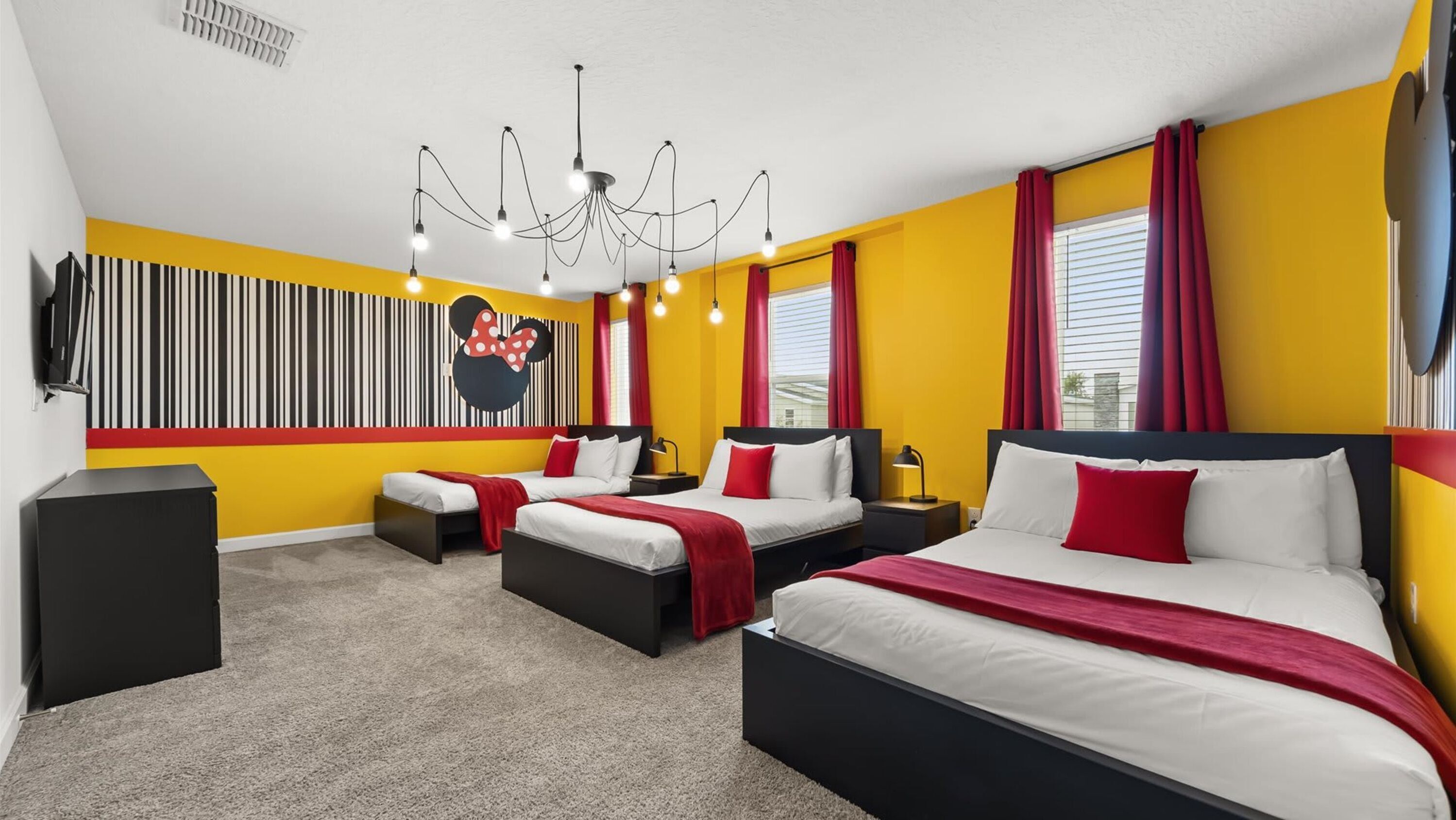 A hotel room with two beds, a Mickey Mouse mural, a chandelier, and red curtains.