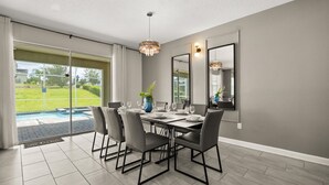 A dining area with a pool view, grey walls, and modern furniture. - Upstay Championsgate 9BR Villa With Pool Cinema (Davenport)
