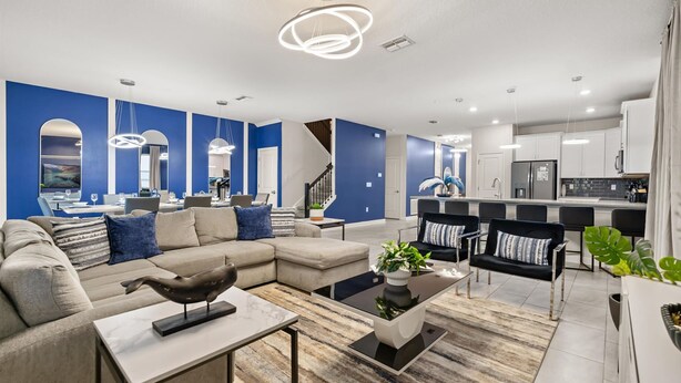 A modern living room with a sectional sofa, a coffee table, and a dining area with chairs and a TV. - Upstay Championsgate 9BR Villa With Pool Cinema (Davenport)