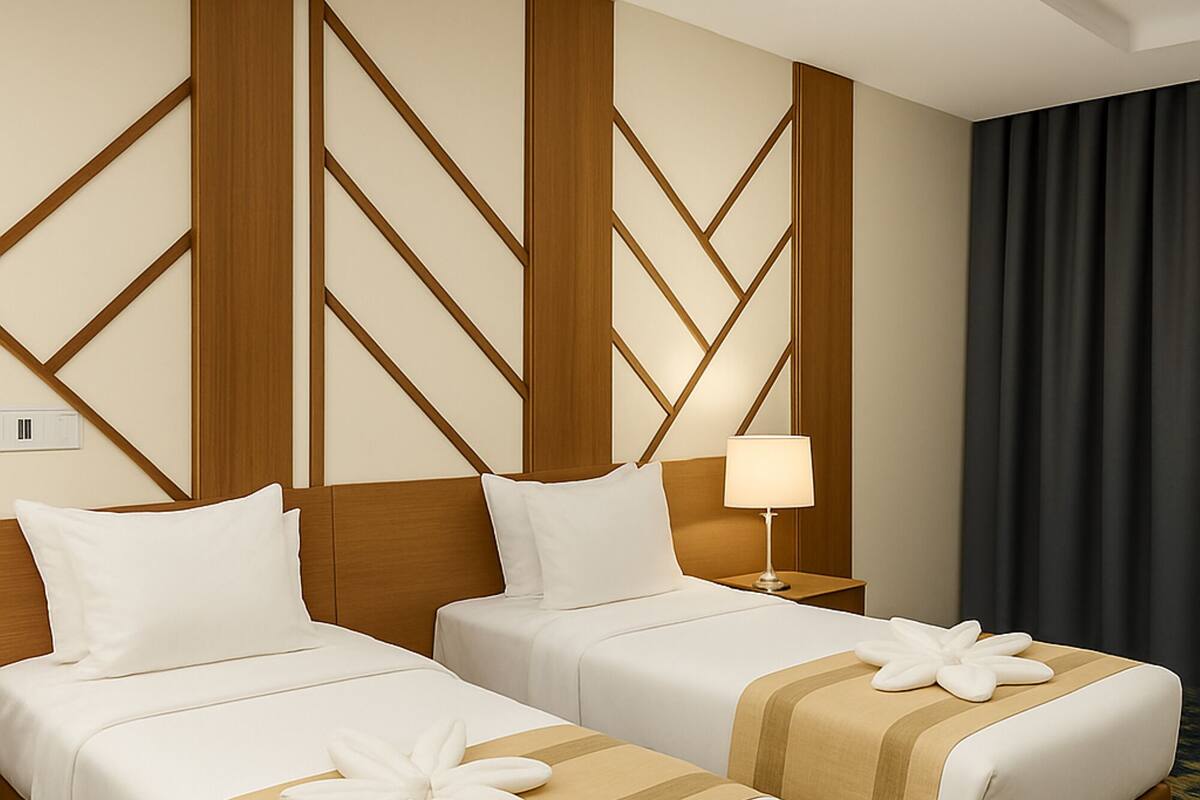 Ein Hotelzimmer mit zwei Betten, Holz-Kopfteilen, einem Nachttisch mit Lampe und einem dunklen Vorhang.