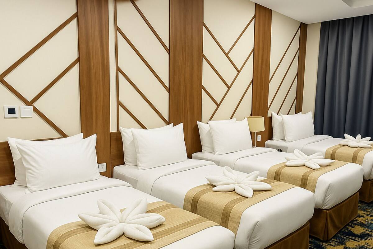 Ein Hotelzimmer mit vier nebeneinanderliegenden Betten, jedes mit weißer Bettwäsche und braunen Akzenten.