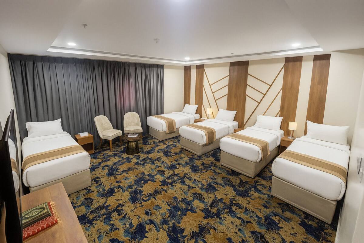 Ein Hotelzimmer mit vier Betten, einem Fernseher, einem Schreibtisch und einem Stuhl.
