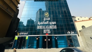 A tall hotel with a modern glass facade and a prominent logo. - Moro Alalameyah Hotel Makkah (Makkah)