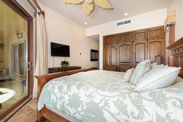 A bedroom with a large bed, wooden wardrobe, and a television on the wall.