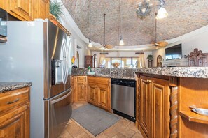 A kitchen with wooden cabinets, stainless steel appliances, granite countertops, and a ceiling with exposed brick.