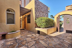 A courtyard with stone flooring, a wooden pergola, and a stone wall.