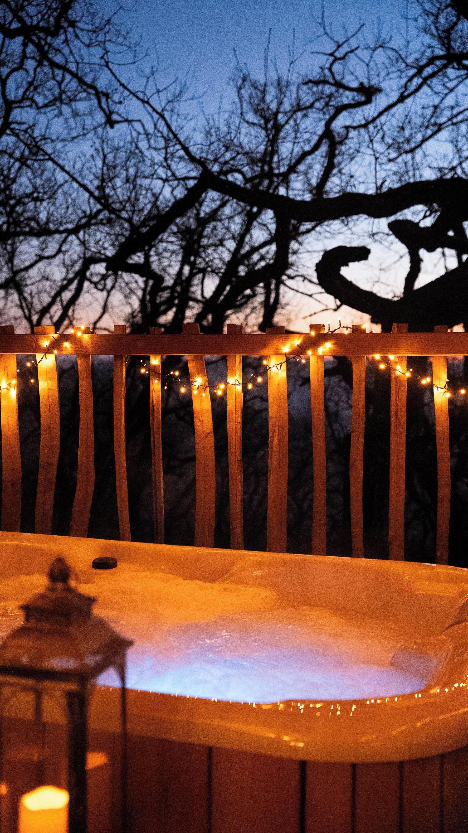 Een houten terras met lichtjes en een hottub.