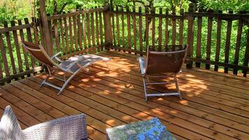 A wooden deck with wicker furniture, including two lounge chairs and a small table, surrounded by a wooden fence and trees.