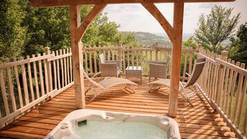 A wooden deck with a hot tub, wicker chairs, and a wooden railing overlooking a scenic landscape.