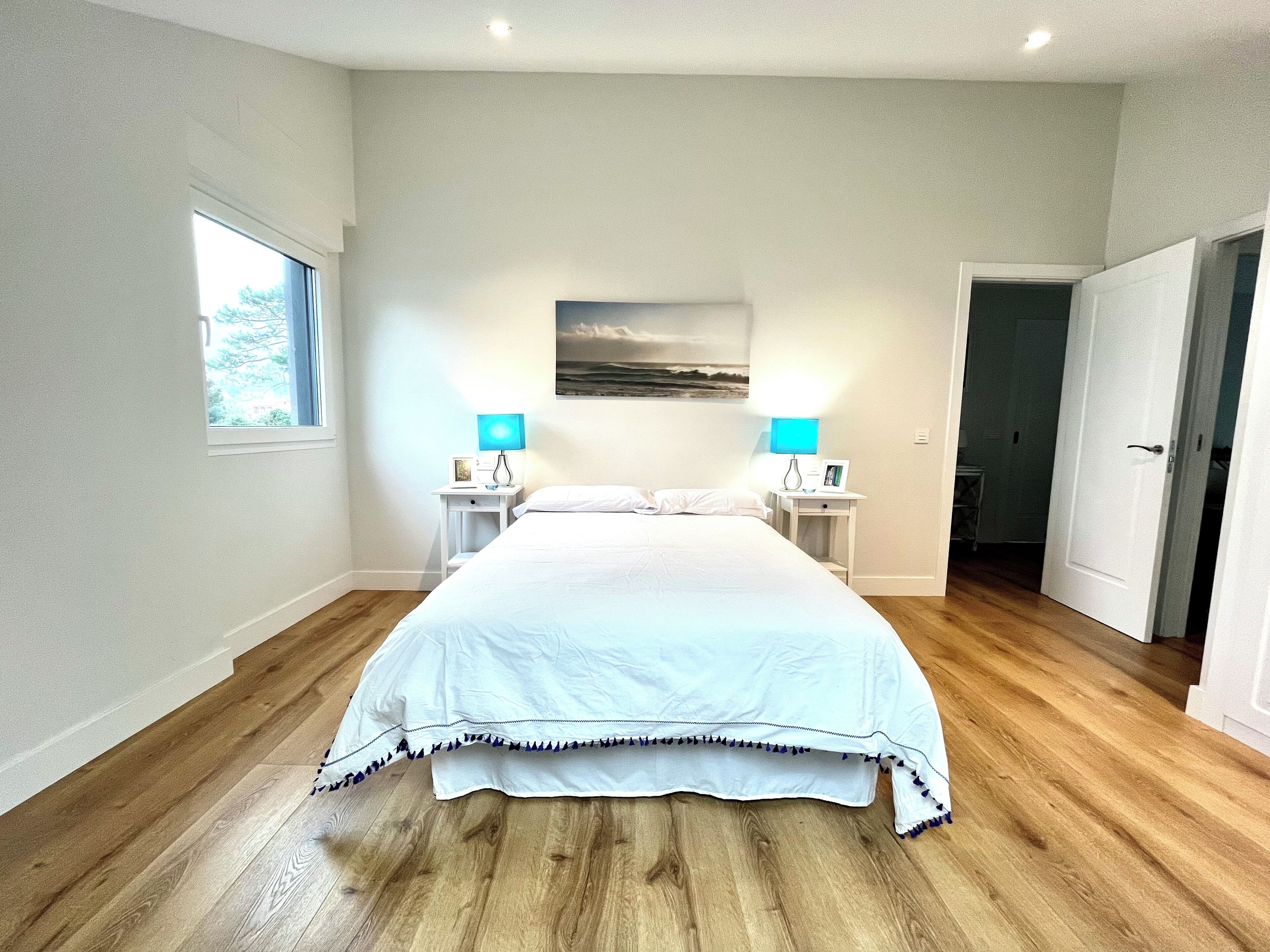 A bedroom with a large bed, two bedside tables with lamps, a window, and a door.