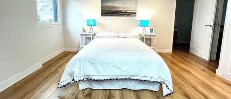 A bedroom with a large bed, two bedside tables with lamps, a window, and a door.