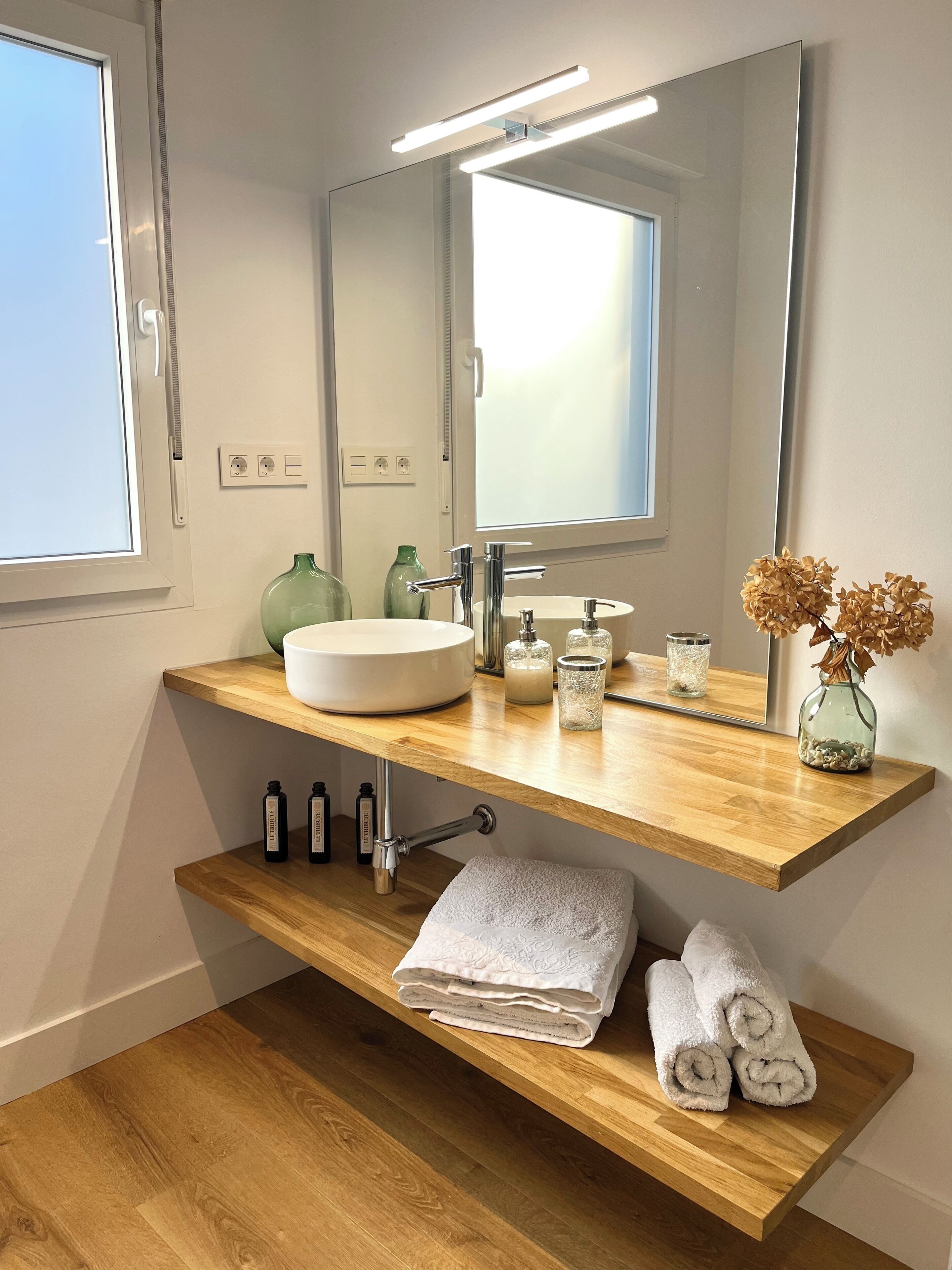 Ein modernes Badezimmer mit einem Holzboden, einem großen Spiegel und einem integrierten Waschbecken.