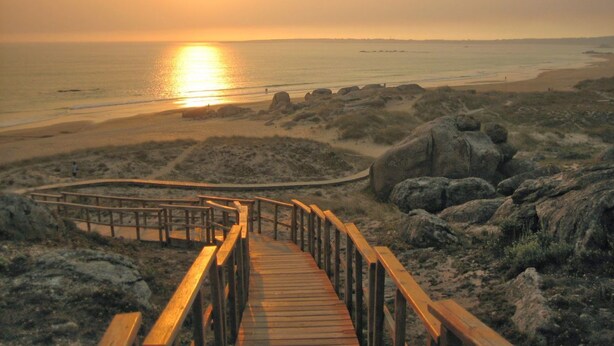 A wooden boardwalk leading to a beach with a sunset in the background.