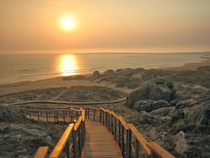 A wooden boardwalk leading to a beach with a sunset in the background. - Beachfront House (Ribeira)