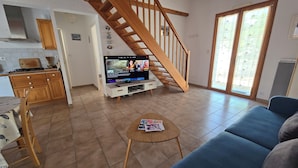 A living room with a TV, wooden staircase, and a dining area. - Beach house, a stone's throw from the sea and the pine forest (La Tranche-sur-Mer)