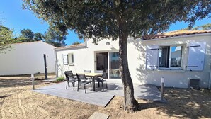 A white house with a tiled roof, a patio with a table and chairs, and a tree in front. - Beach house, a stone's throw from the sea and the pine forest (La Tranche-sur-Mer)