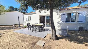 Una casa blanca con techo de tejas, un patio con mesa y sillas, y un árbol al frente.