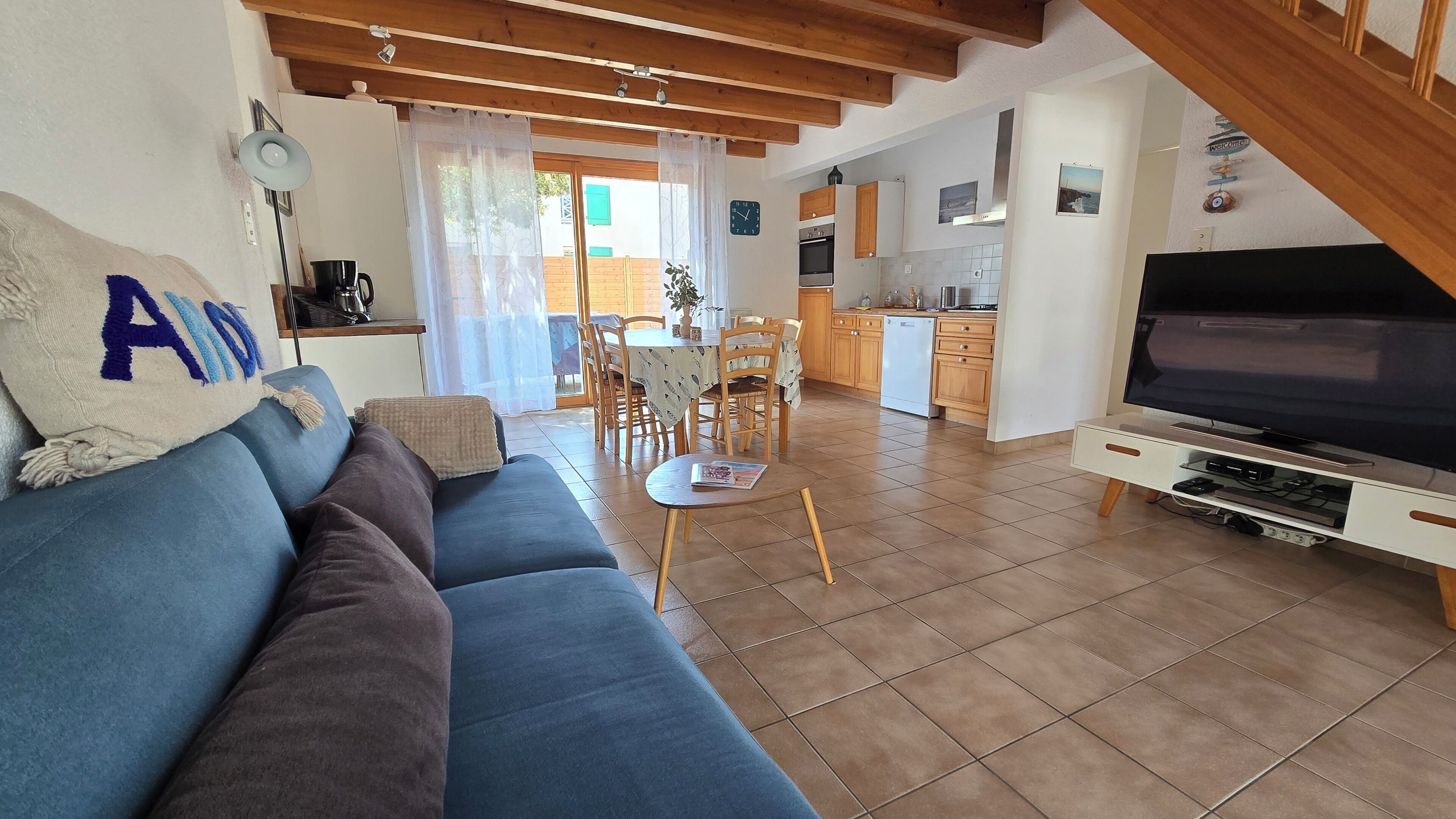 Una sala de estar con sofá, mesa de centro, televisor y una cocina al fondo.