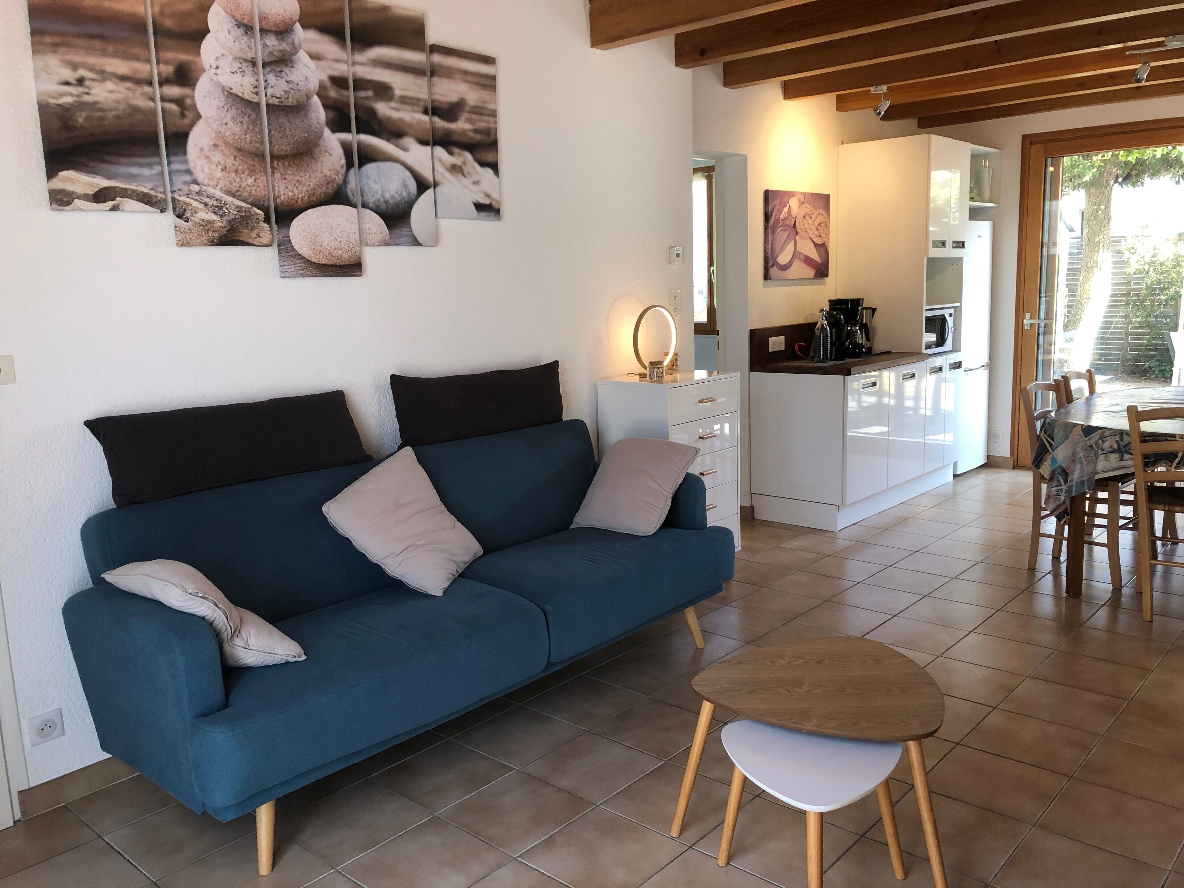 A modern living room with a blue sofa, a small round table, and a kitchen in the background.