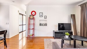 Un salon moderne avec un plancher en bois, une échelle rouge, un téléviseur et un canapé.
