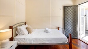 A neatly made bed with white linens and a rolled towel, a bedside lamp, and a view of a door with a metal security screen.