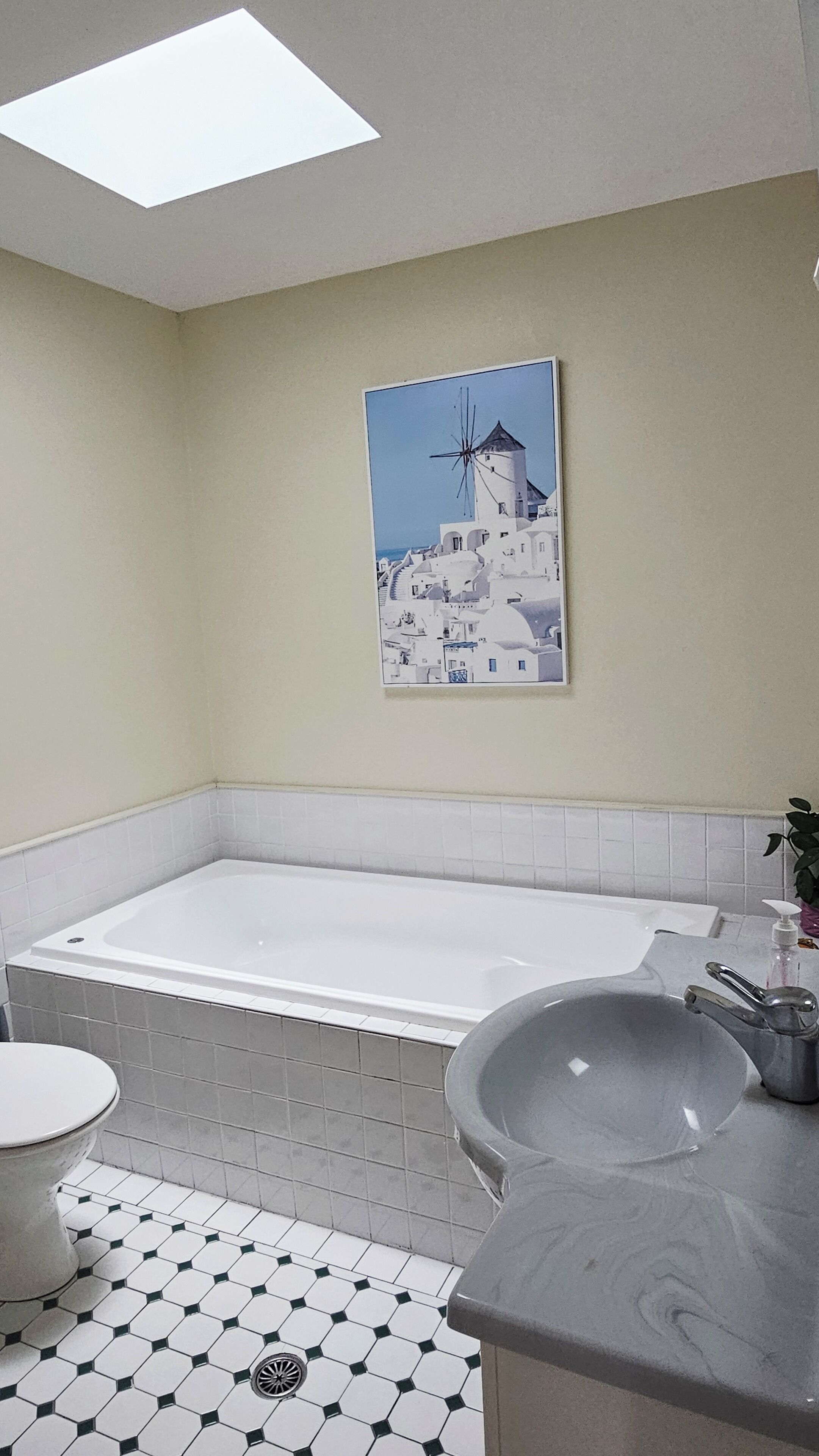 A bathroom with a large bathtub, a toilet, a sink, and a skylight.