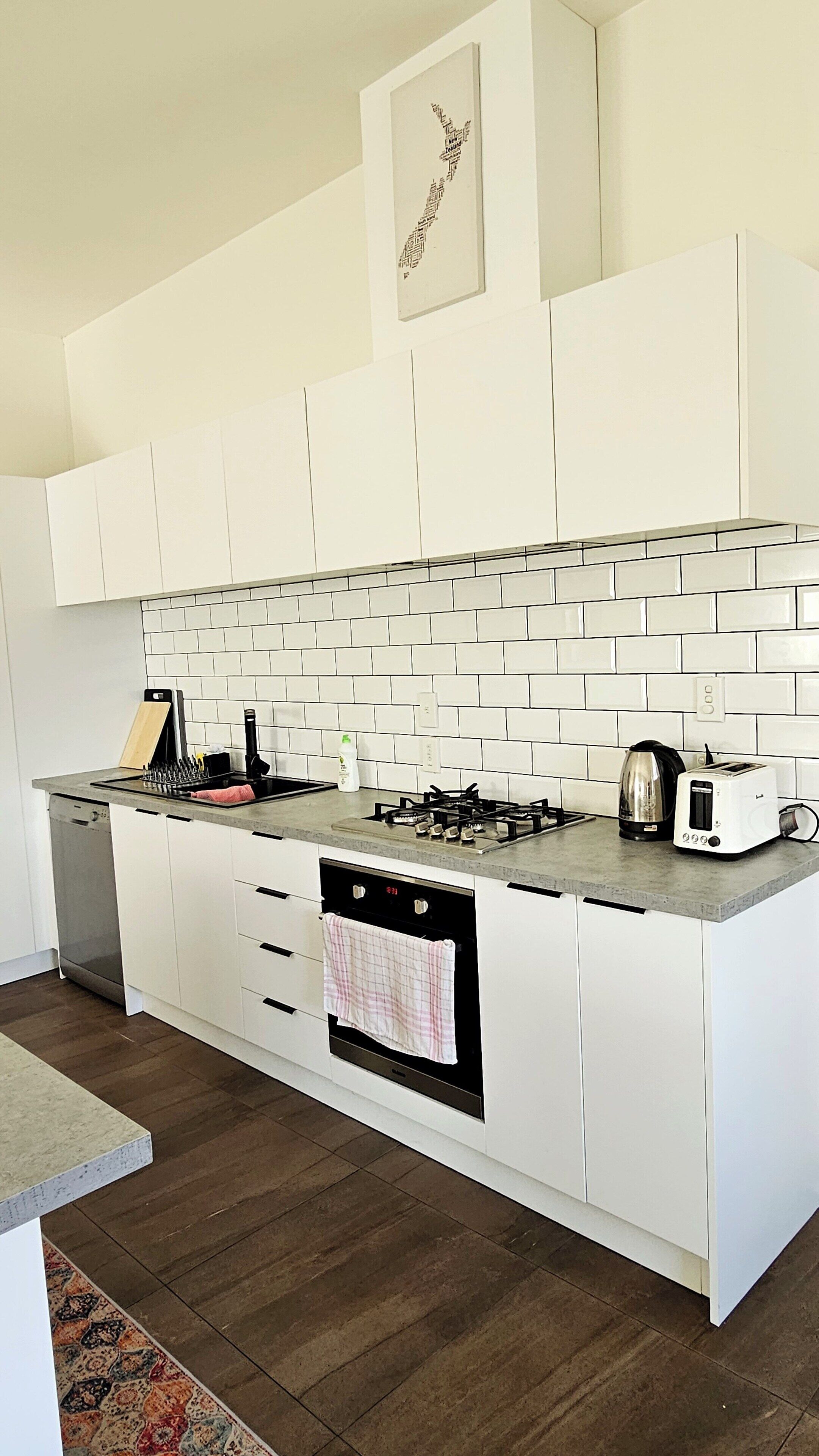A modern kitchen with white cabinetry, a tiled backsplash, a gas stove, a built-in oven, and a toaster.