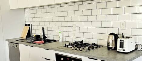 Une cuisine moderne avec des meubles blancs, un pare-feu en carrelage, une cuisinière à gaz, un four encastré et un grille-pain.
