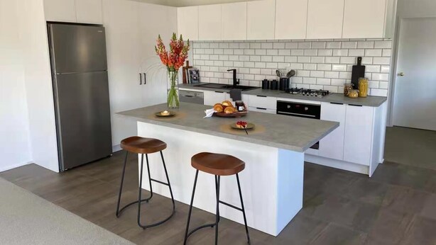 A modern kitchen with white cabinetry, a stainless steel refrigerator, a central island with stools, and a tiled backsplash. - LILYPAD 4-bedroom Urban Retreat Auckland (Auckland)
