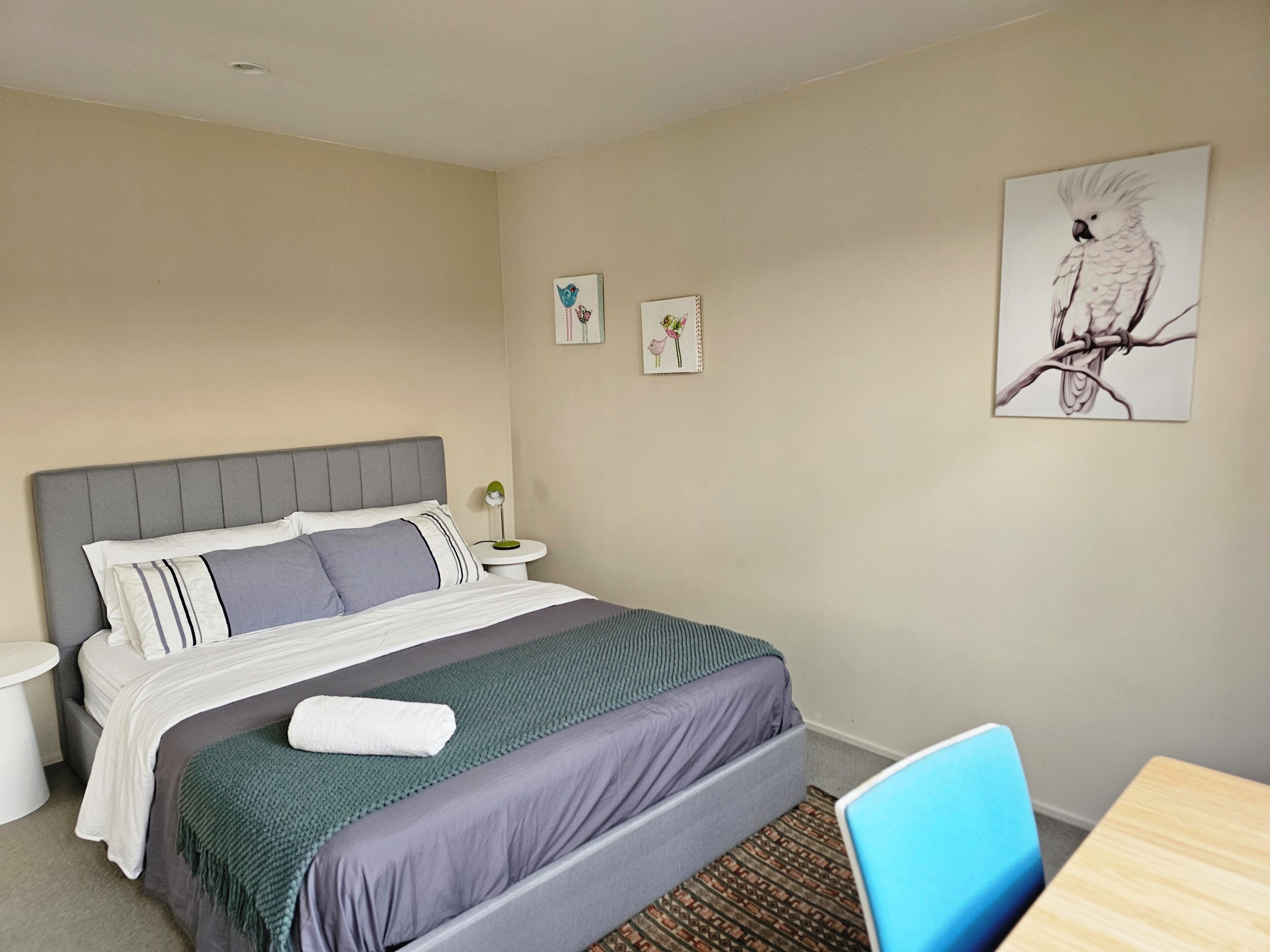 A bedroom with a bed, bedside table, lamp, and a framed artwork on the wall.