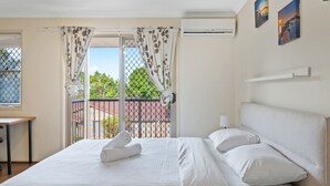Een hotelkamer met een bed, een bureau en een balkon met uitzicht op de stad.
