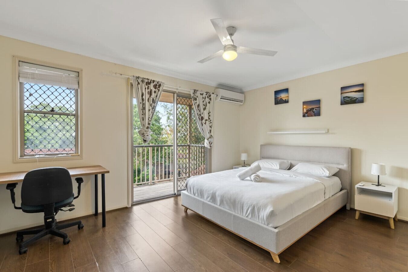 A bedroom with a bed, a desk, a chair, a ceiling fan, and a window with curtains.