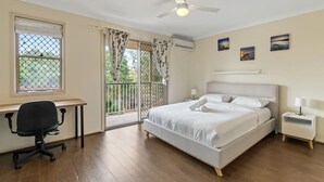 Een slaapkamer met een bed, een bureau, een stoel, een plafondventilator en een raam met gordijnen.