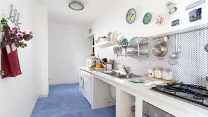 A kitchen with a blue tiled floor, white cabinets, a stainless steel sink, and a gas stove. - Sea Scent - My Rental Homes (San Montano)