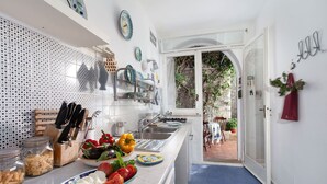 A kitchen with a long countertop, various utensils, and fresh vegetables. - Sea Scent - My Rental Homes (San Montano)