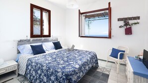 A bedroom with a bed, a chair, a desk, and a window with a view. - Sea Scent - My Rental Homes (San Montano)