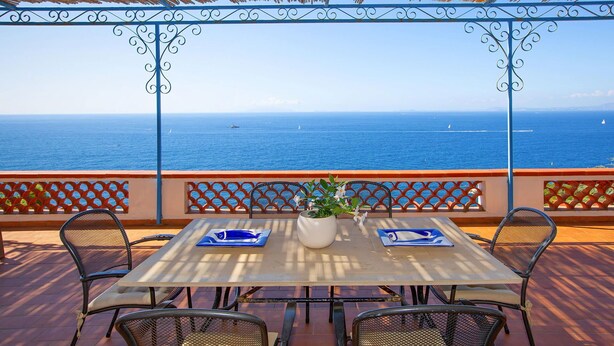 A table with chairs and a potted plant on a terrace overlooking the sea. - Sea Scent - My Rental Homes (San Montano)