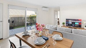Un coin repas avec une table dressée pour quatre personnes, un canapé gris et un téléviseur affichant l’interface d’un service de diffusion en continu.