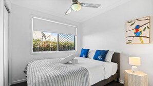 Une chambre d’hôtel moderne avec un grand lit, un ventilateur de plafond, une fenêtre donnant sur un paysage verdoyant et un tableau représentant un oiseau accroché au mur.