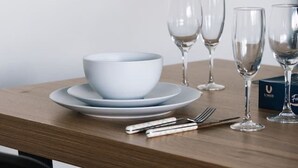 Une table à manger avec un saladier blanc, des assiettes, des couverts et des verres à vin.