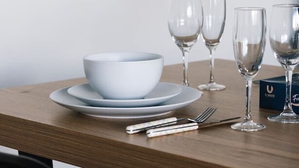Une table à manger avec un saladier blanc, des assiettes, des couverts et des verres à vin.