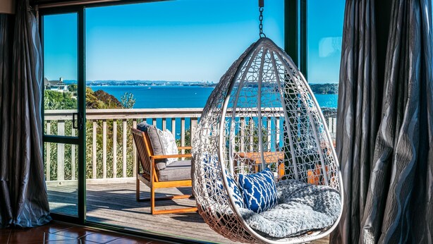 A hanging chair on a balcony with a view of the sea and a cityscape.
