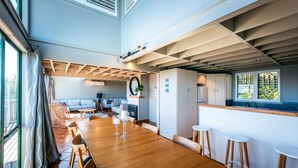 A spacious dining area with a long wooden table, bar stools, and a kitchen area with a window.