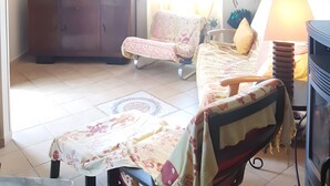 Ein Wohnzimmer mit Fernseher, Sofa, Sessel, Schrank und einem fenster mit Vorhängen.