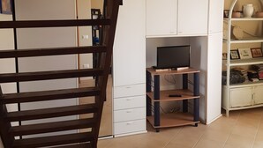 Eine Treppe führt zu einem Raum mit einem Fernseher, Schränken und einem Regal mit Büchern und Dekorationsgegenständen.