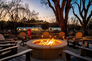 A fire pit surrounded by Adirondack chairs, a red telephone booth, and a camper parked in the background.