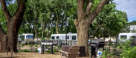 Un camping con vehículos recreativos, una parrilla y un banco.