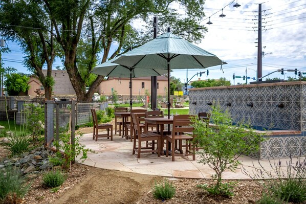 Une terrasse extérieure avec des tables et des chaises en bois, un grand parasol et un mur décoratif recouvert de carreaux.